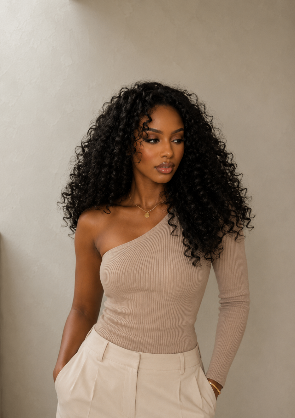 Editorial portrait with deep, defined curls against a neutral wall